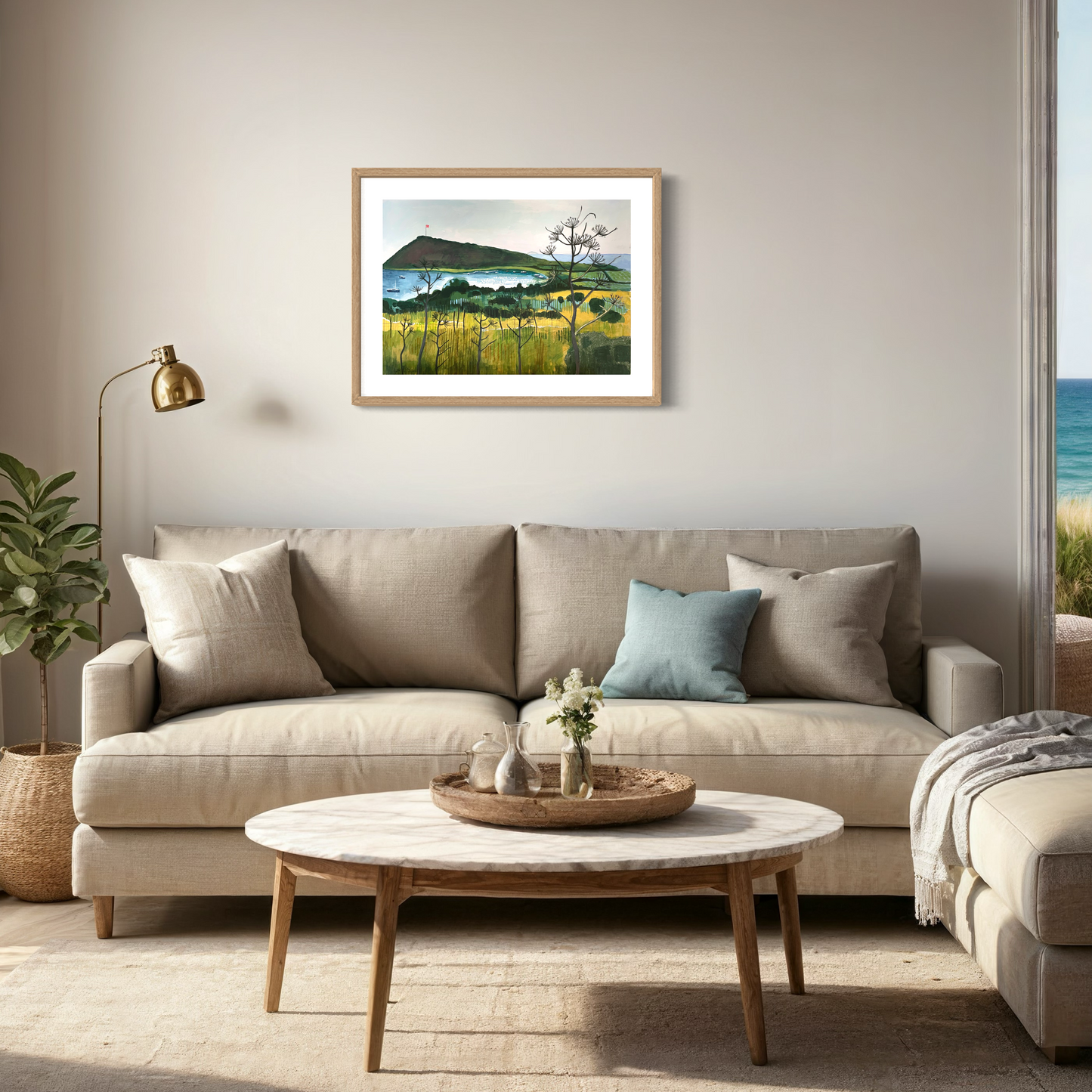 Aegean Autumn landscape by Elaine Boylan. View of Gümüşlük bay on the Bodrum Peninsula in Turkey. Pale blue sky, turquoise sea, hill with flag pole flying the Turkish flag, field in the foreground. Colours are mainly greens, golds and blues. High quality giclée print on fine art paper with mount/mat and classic natural wood frame. Print is shown in a cosy neutral room above a sofa and coffee table