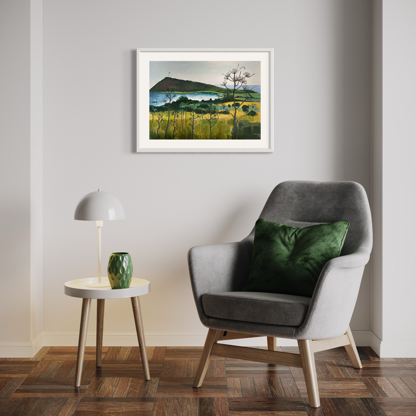 Aegean Autumn landscape by Elaine Boylan. View of Gümüşlük bay on the Bodrum Peninsula in Turkey. Pale blue sky, turquoise sea, hill with flag pole flying the Turkish flag, field in the foreground. Colours are mainly greens, golds and blues. High quality giclée print on fine art paper with mount/mat and classic white frame. Print is shown in a room above a chair and side table.