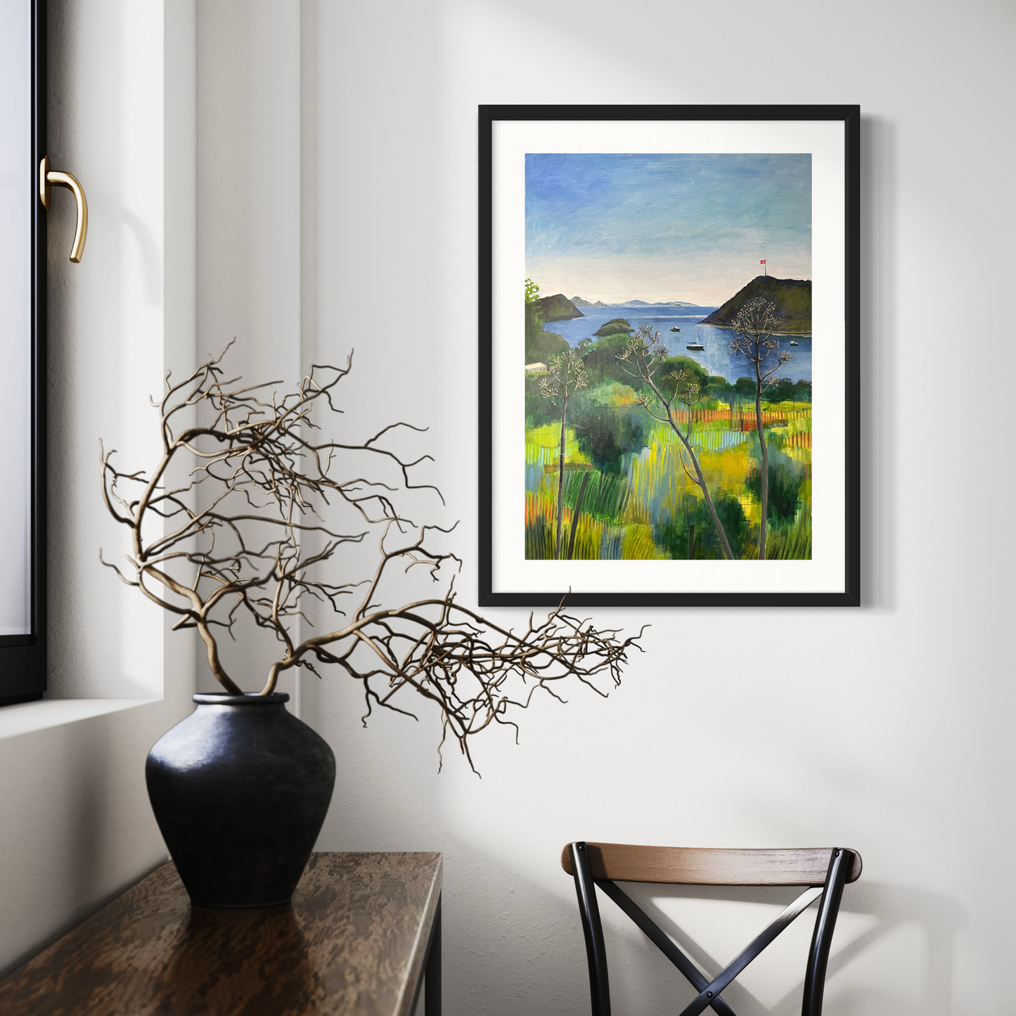 After the Rain landscape by Elaine Boylan. View from Gümüşlük on the Bodrum Peninsula in Turkey. Pale blue sky over the Aegean sea, hill with flag pole flying the Turkish flag, field in the foreground, Greek islands in the distance. Colours are mainly greens, golds and blues. High quality giclée print on fine art paper with mount/mat and black frame. Print is shown in a bright hallway behind a console table with a vase of twigs.