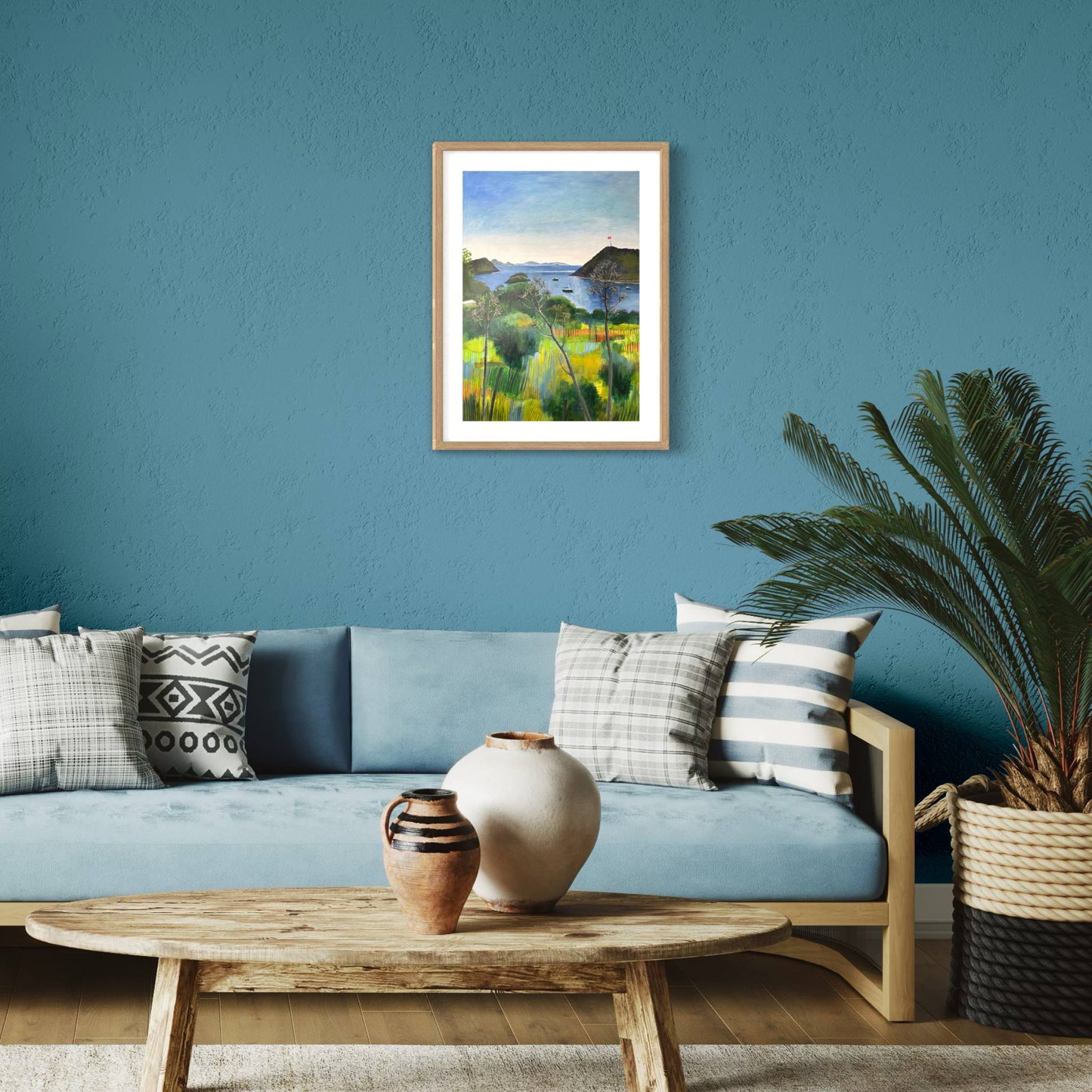 After the Rain landscape by Elaine Boylan. View from Gümüşlük on the Bodrum Peninsula in Turkey. Pale blue sky over the Aegean sea, hill with flag pole flying the Turkish flag, field in the foreground, Greek islands in the distance. Colours are mainly greens, golds and blues. High quality giclée print on fine art paper with mount/mat and natural wood frame. Print is shown in a contemporary style room on a teal wall above a pale blue sofa.
